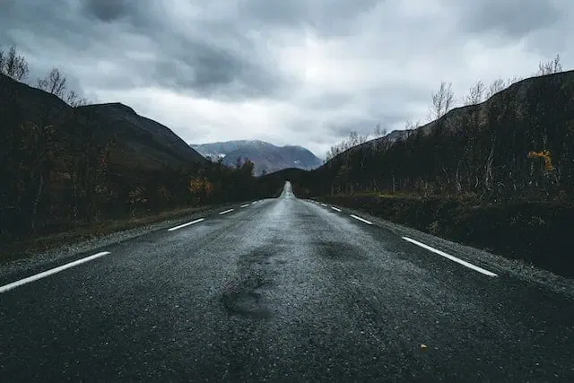 Dark forested mountain road with cloudy sky, no traffic, moody landscape, scenic drive, outdoor transportation, nature surroundings.