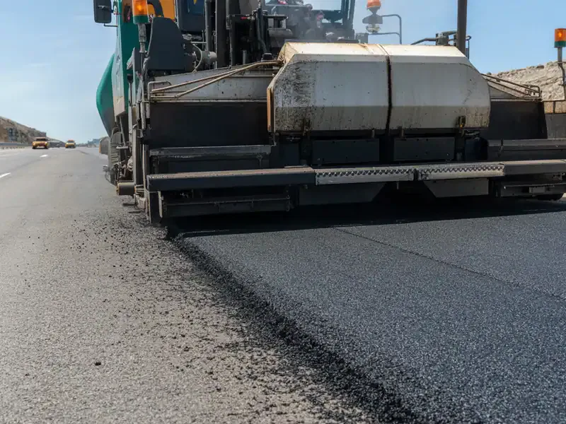 Asphalt paving machine laying fresh road surface on highway construction site
