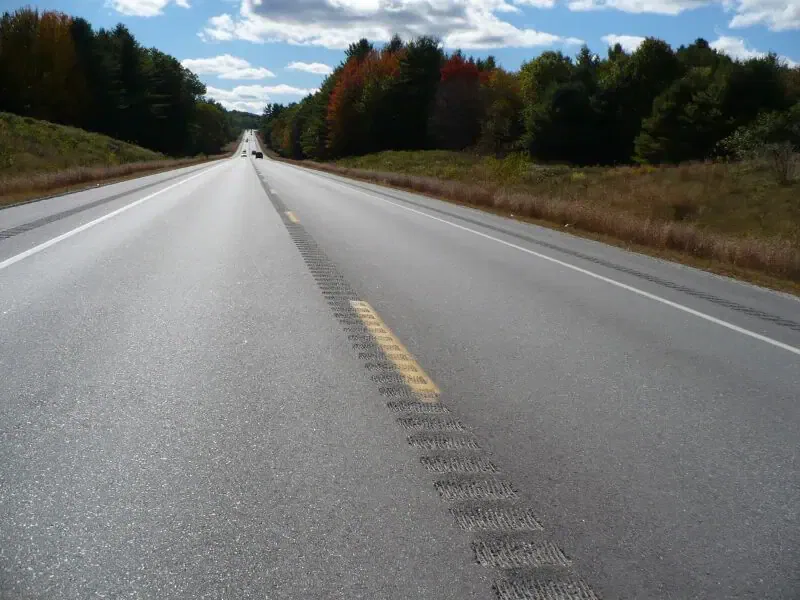 Rural highway with rumble strips down center line, autumn trees lining both sides of road