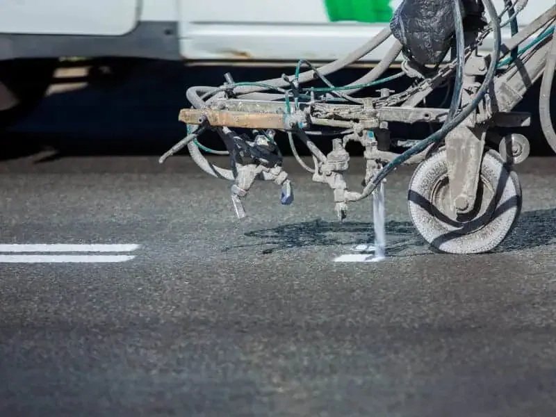 Industrial road striping equipment with spray nozzles painting white lines on dark asphalt pavement