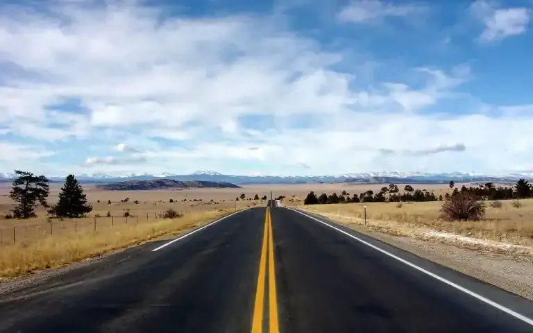 Straight highway stretching toward distant mountains under blue sky with grasslands